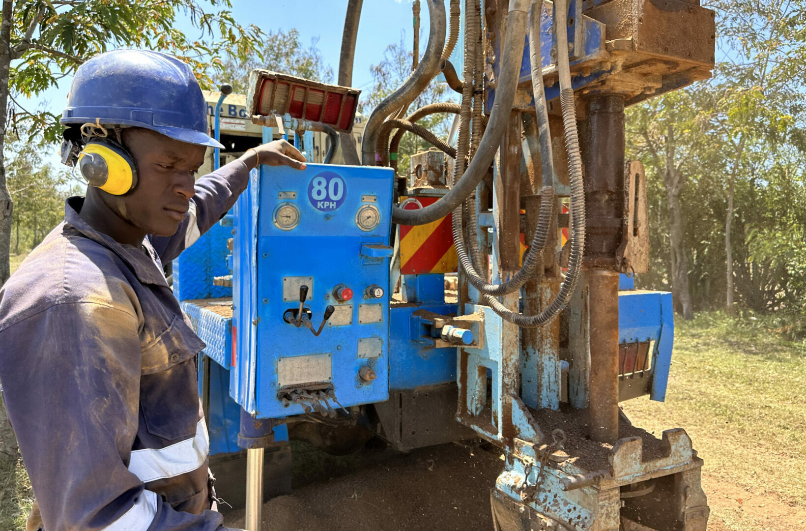 A local drilling team member, clad in a dusty uniform, operates heavy drilling machinery for constructing a well, demonstrating commitment to sustainable water solutions.