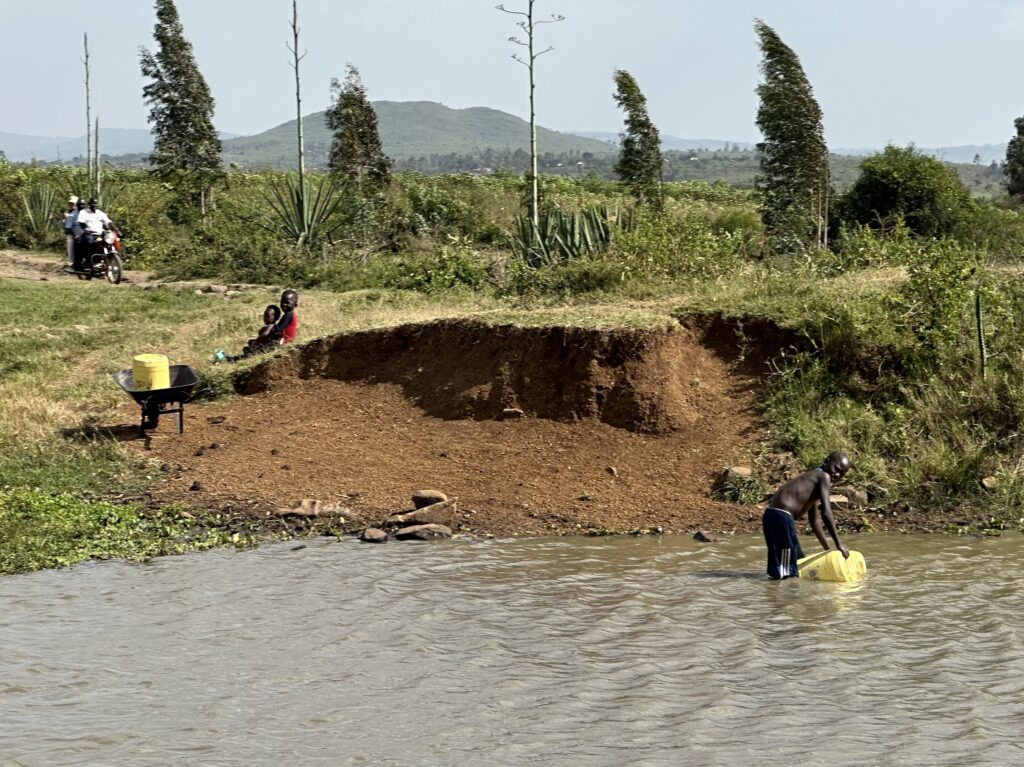 Ein Junge schöpft Wasser aus einem unsicheren Fluss in Afrika, während Kinder am Ufer sitzen. Fehlende Brunnen zwingen Millionen Menschen dazu, verschmutztes Wasser zu nutzen – mit fatalen Folgen für Gesundheit und Leben. Der Weltwassertag macht auf diese Krise aufmerksam und zeigt, wie Brunnenbau in Afrika nachhaltige Lösungen schafft.