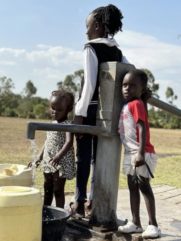 Drei Kinder stehen an einer Wasserpumpe in Afrika und schöpfen sauberes Wasser aus einem neu gebauten Brunnen. Der Brunnenbau in Afrika verändert Leben – er sichert Trinkwasser, verbessert Hygiene und gibt Kindern eine Zukunft.