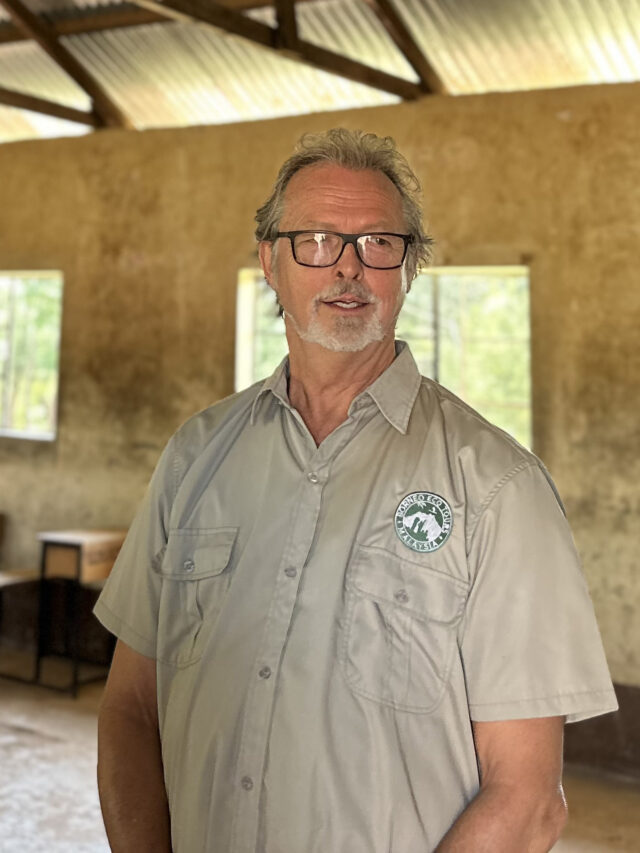 Chris Dann of WellBoring, responsible for legacy donations, events, and member relations, stands poised in a school setting, symbolizing commitment to sustainable development.