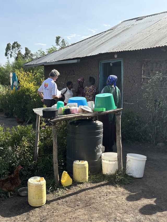 WellBoring team members engage with teachers at a Kenyan homestead, examining a typical washing station for kitchenware and general hygiene.