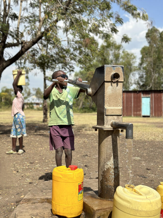 A young person vigorously operates a hand pump, joyously drawing clean water, a testament to WellBoring's sustainable impact.