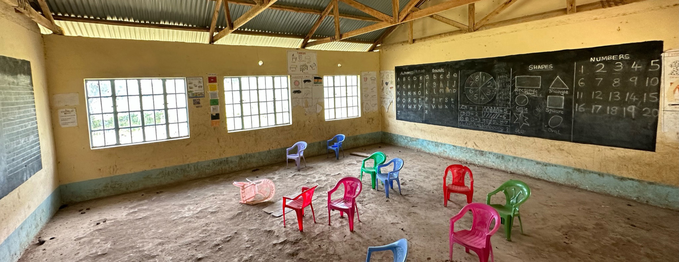 An evocative image of a Kenyan classroom with overturned chairs on a dusty clay floor, symbolizing the stark educational needs.