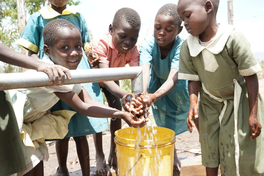 A group of African children delight in the clean water from a WellBoring well, washing their hands and embracing hygiene practices.