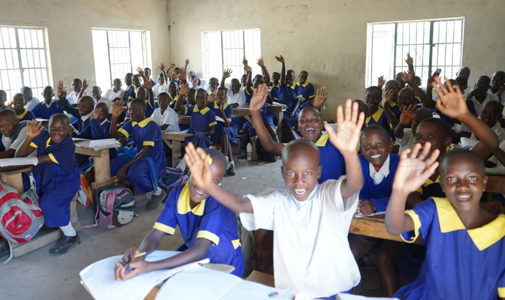 Enthusiastic schoolchildren in uniforms waving in a well-maintained classroom, a testament to the positive impact of safe water access on their education and health.