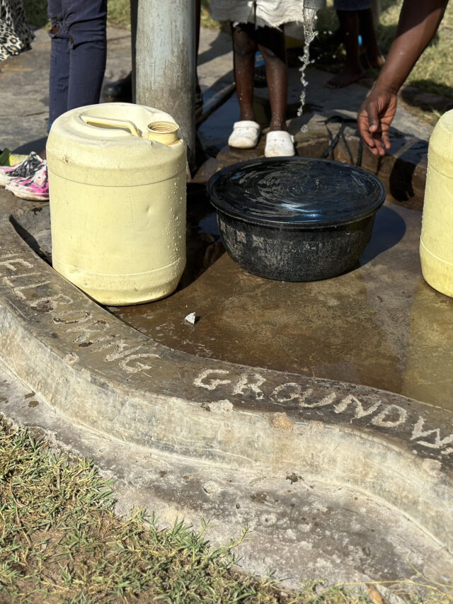 The concrete foundation of a handpump well at a primary school, etched with 'WellBoring Groundwater' to signify the provider of this essential water source.