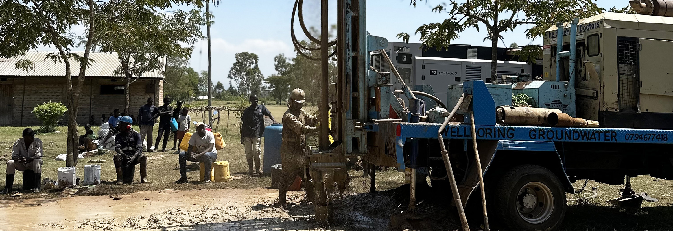 Groundwater drilling team in action, with Stephen Omondi operating the rig and others assisting, set against a rural school backdrop.